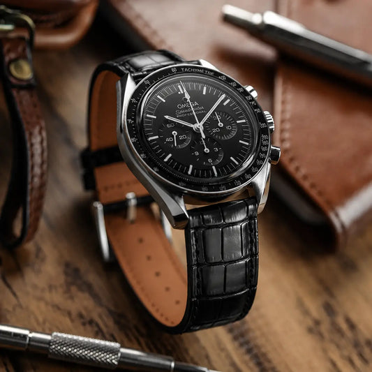 Luxury black crocodile embossed leather watch strap with a semi-gloss finish, shown on an Omega Speedmaster Professional Moonwatch with a stainless steel buckle.