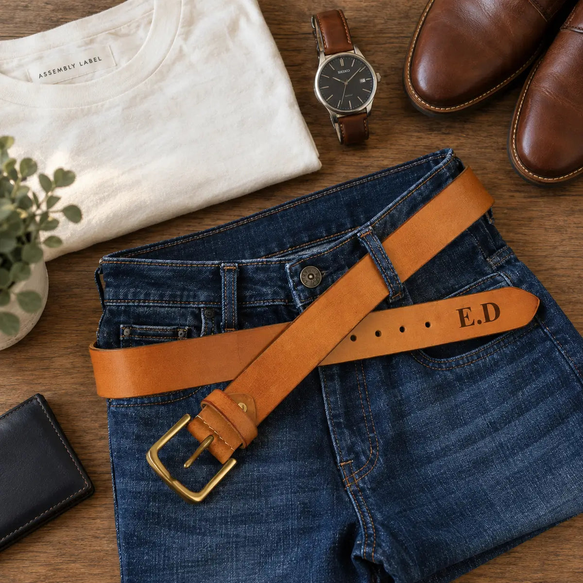Personalised brown leather men’s belt with brass buckle styled with blue jeans, shirt, watch and brown leather shoes.