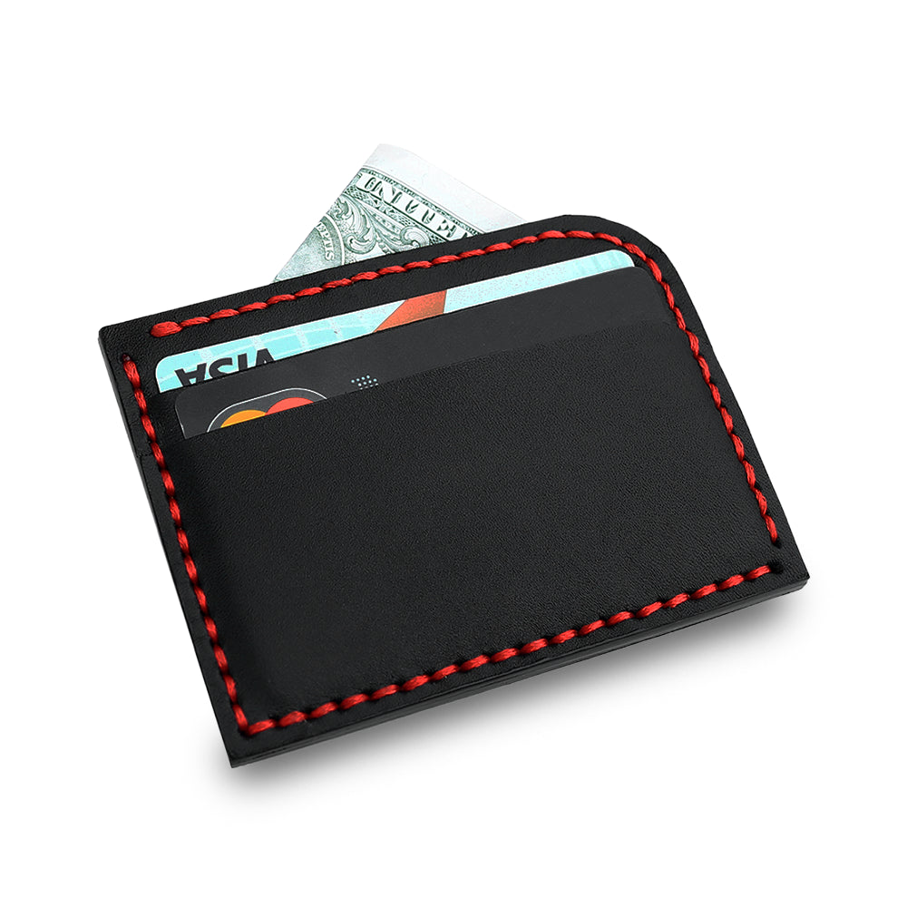Black leather cardholder with red stitching holding cards and cash, placed on a wooden desk beside a laptop and notebook.