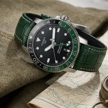 Tissot Seastar GMT watch with a handcrafted green crocodile leather watch strap displayed on a vintage topographic map beside a brass compass, highlighting luxury craftsmanship and travel-ready elegance.