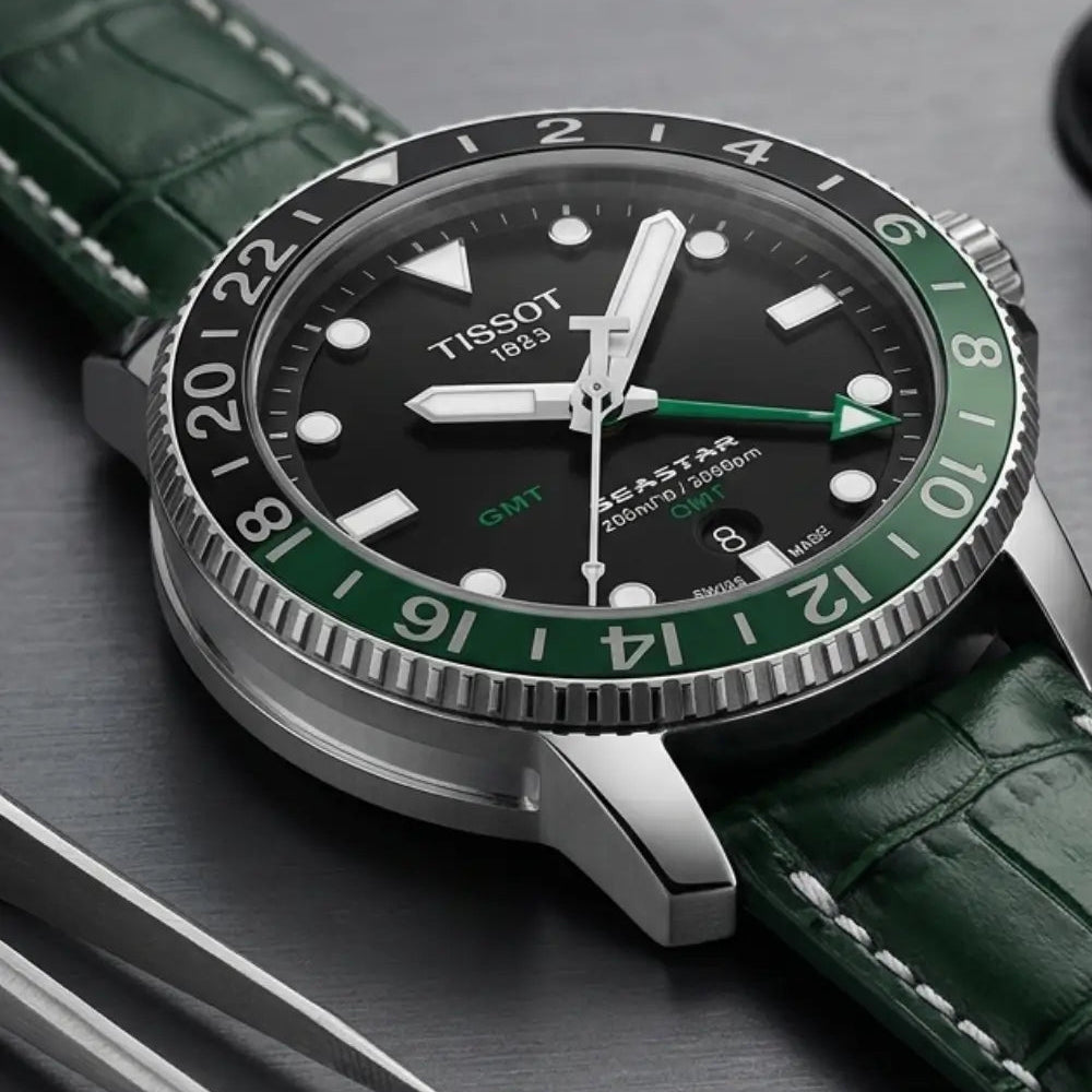 Macro close-up of a Tissot Seastar GMT watch paired with a green crocodile leather watch strap, displayed beside precision watchmaking tweezers to emphasize premium leather texture, fine stitching, and artisan craftsmanship.
