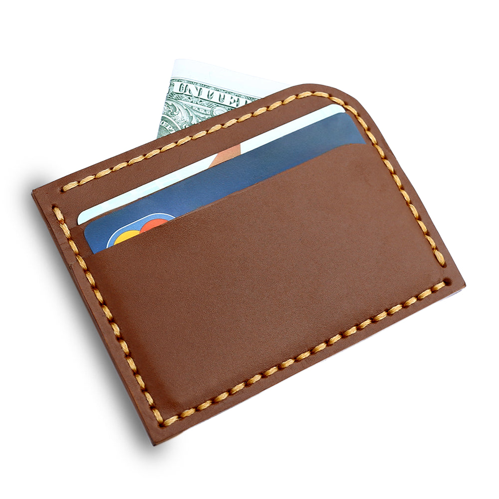 Tan leather cardholder with visible stitching holding multiple cards, placed on a rustic wooden table beside a cup of coffee, stacked books, and a pen.