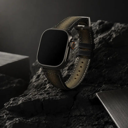 Premium product campaign image of an Apple Watch Ultra fitted with a khaki canvas strap, positioned diagonally against matte black volcanic stone. Soft directional light from the upper left reveals the strap’s natural khaki tone, fine stitching, and brushed titanium details while preserving deep shadows and cinematic depth. The display remains fully black for a minimalist luxury presentation.