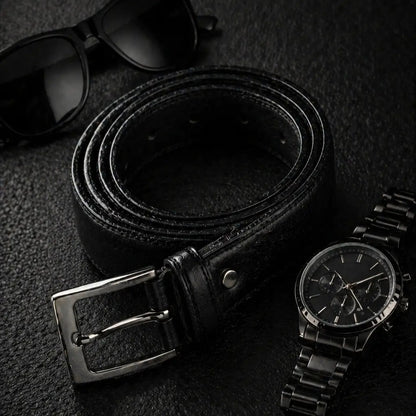 Black leather men’s belt with silver buckle styled beside black sunglasses and a black wristwatch on a dark textured surface.