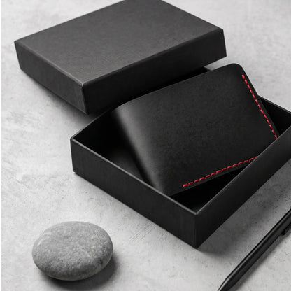 Hand holding an open black bifold leather wallet with bold red stitching, multiple card slots, and cash inside while standing in a city street, highlighting the wallet's slim design and everyday functionality.