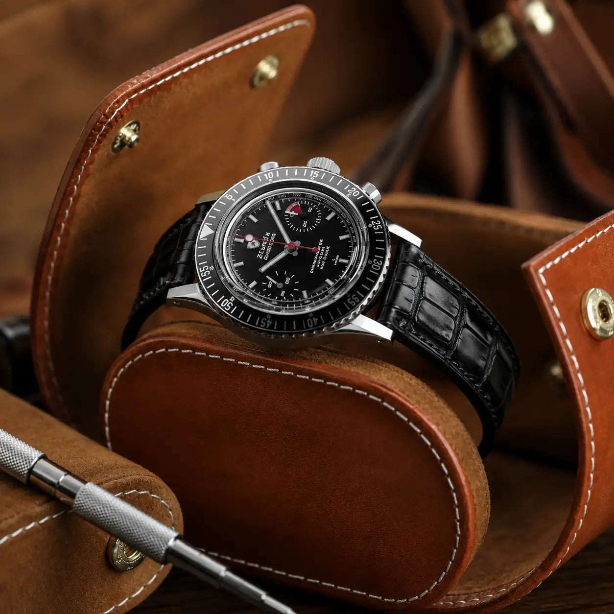 Premium black crocodile leather watch strap with a semi-gloss finish, fitted to a Nivada Grenchen Chronomaster and displayed in a tan leather watch roll.