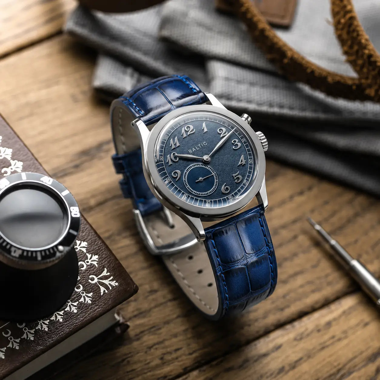 Navy blue crocodile leather watch strap with a glossy finish and square scales, shown on a Baltic Bicompax watch with a matching blue sector dial.