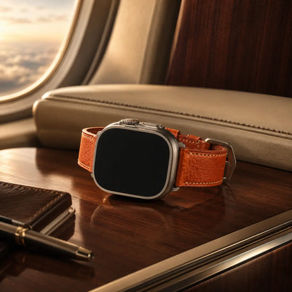 Apple Watch Ultra with a cognac leather strap displayed on a polished walnut surface inside a luxury private jet cabin. Golden-hour light streams through the window, illuminating the textured leather, cream upholstery, and premium materials while the watch screen remains fully black and inactive.