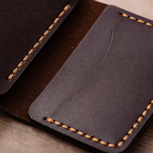 An open-flat view of a tan full-grain leather bifold cardholder against a white background, demonstrating the dual-sided internal card slots filled with credit cards and secured by precision-engineered saddle stitching.