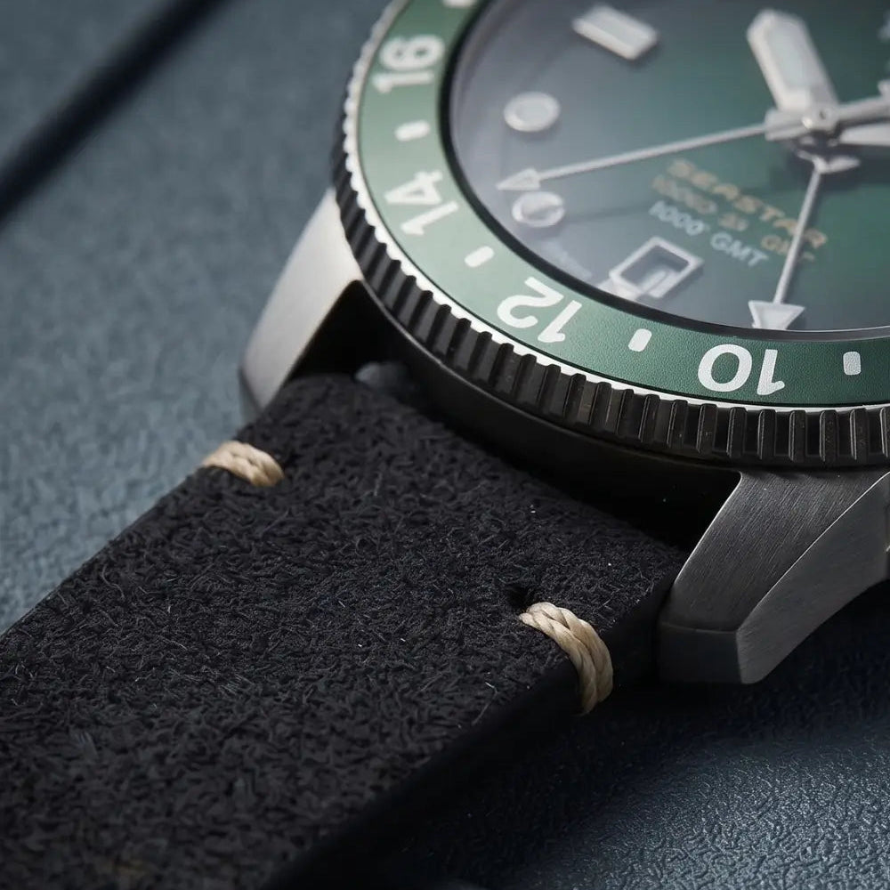 Close-up macro of a black suede leather watch strap attached to a GMT watch, highlighting the soft suede texture, contrast hand stitching, and brushed stainless steel lugs.
