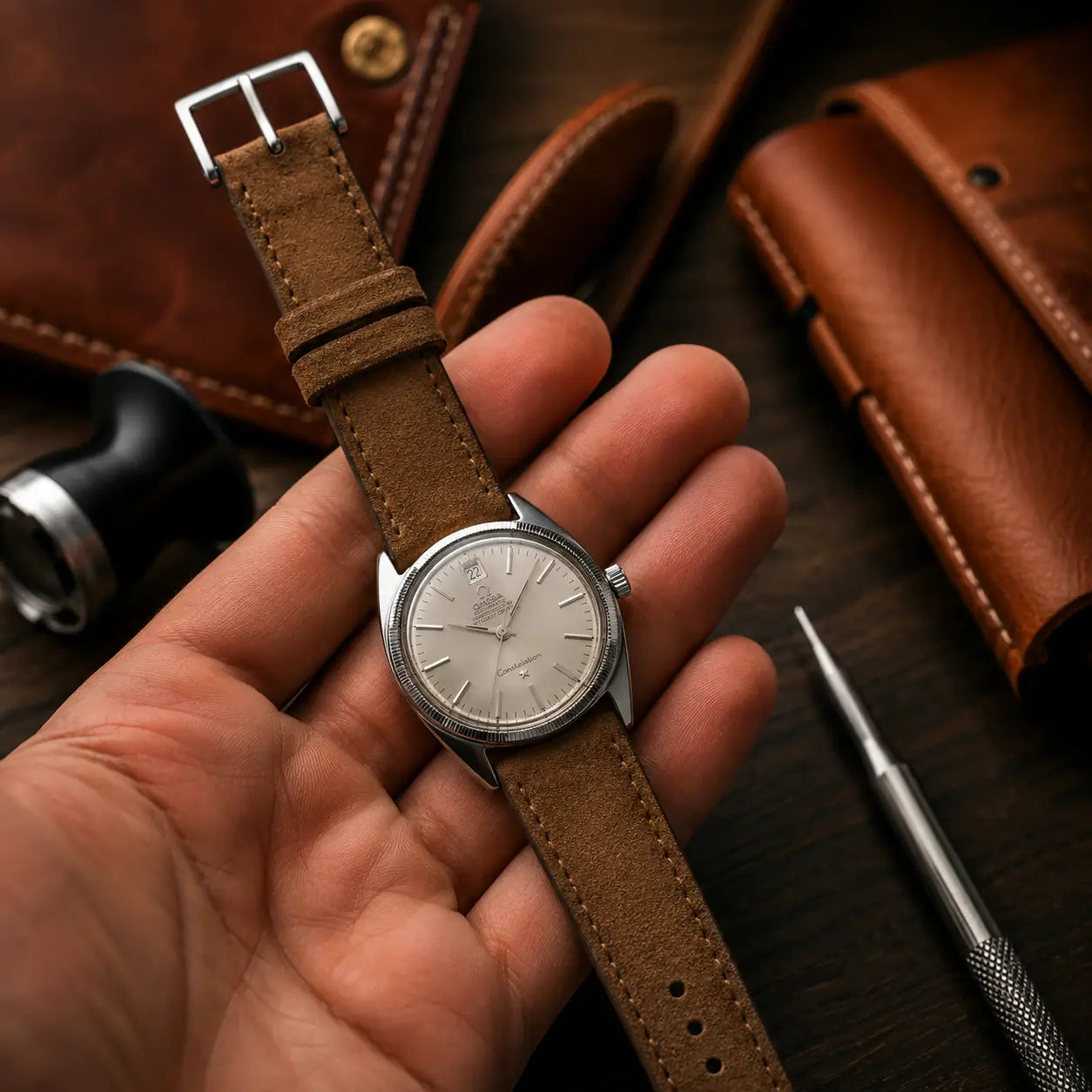 Classic silver dress watch fitted with a dark brown suede leather strap, displayed on a leather watch roll with rich leather props and soft cinematic lighting.