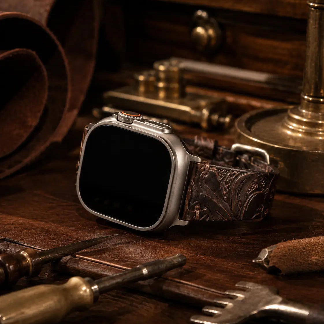 Apple Watch Ultra fitted with a dark brown embossed leather strap displayed on a handcrafted leather workbench surrounded by brass and leatherworking tools. Warm cinematic lighting highlights the engraved floral texture and artisanal luxury aesthetic, while the watch screen remains completely black.
