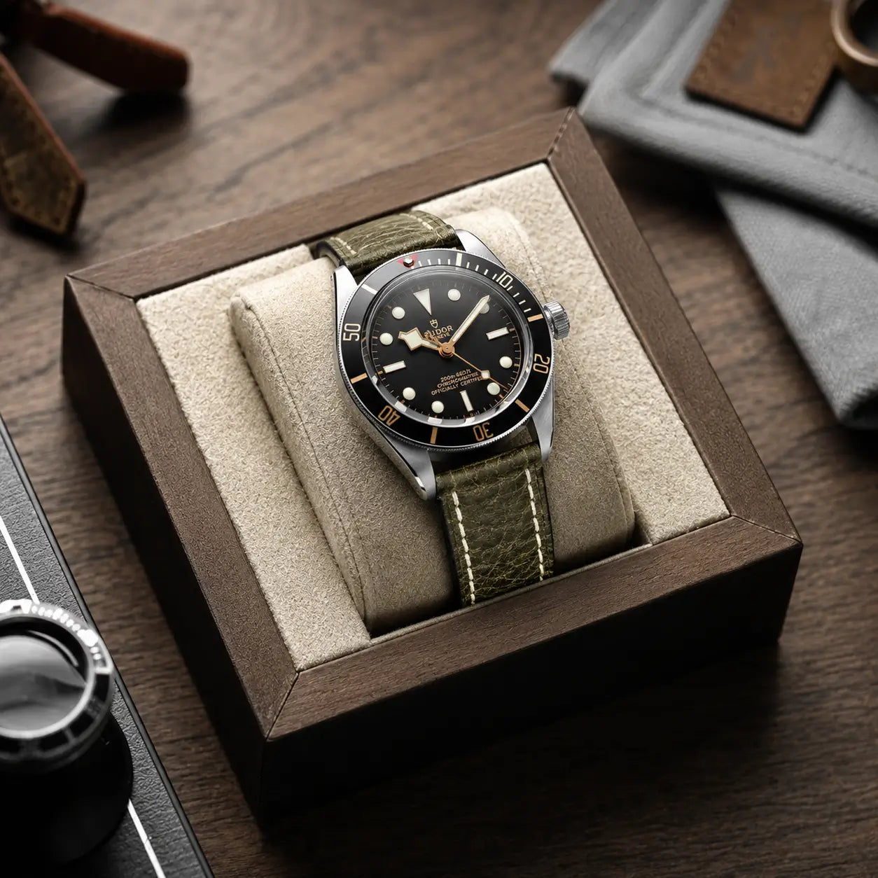 22mm Olive green leather watch strap on Tudor Black Bay watch displayed in a premium watch box, featuring textured leather and contrast stitching.