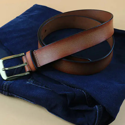 Brown leather men’s belt styled with folded blue clothing showing classic brass buckle