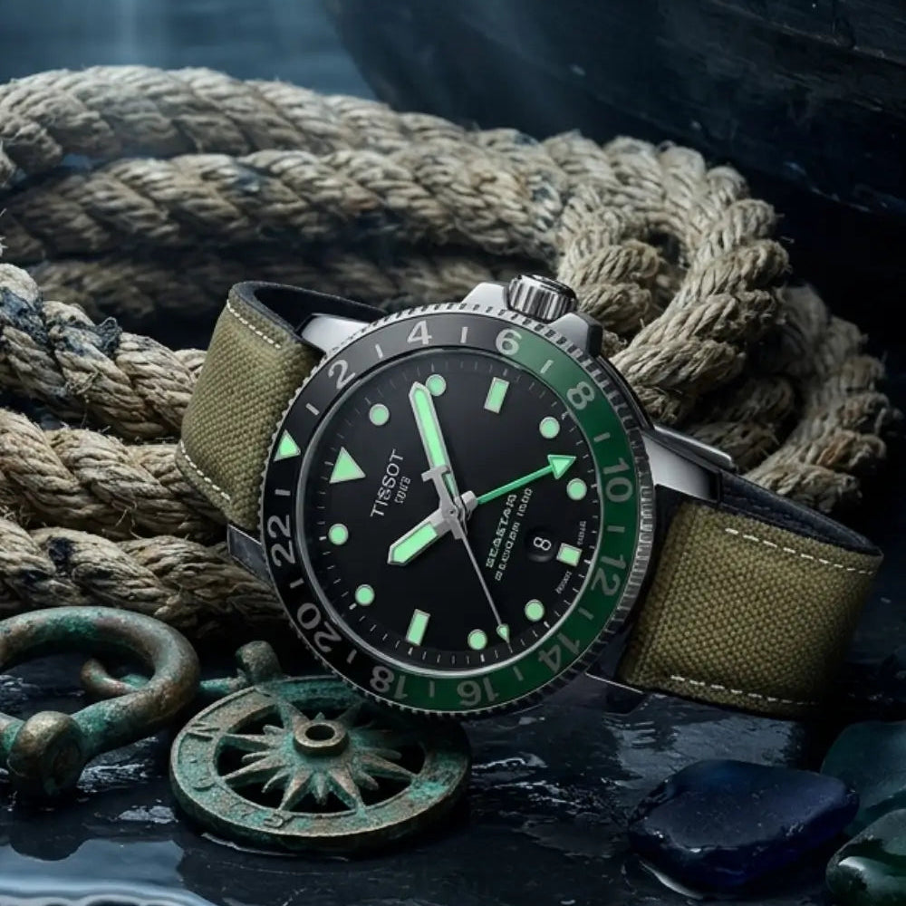 Tissot Seastar GMT watch fitted with a khaki canvas watch strap displayed on a wet stone surface beside nautical rope and vintage maritime hardware, showcasing rugged durability and outdoor-inspired craftsmanship.