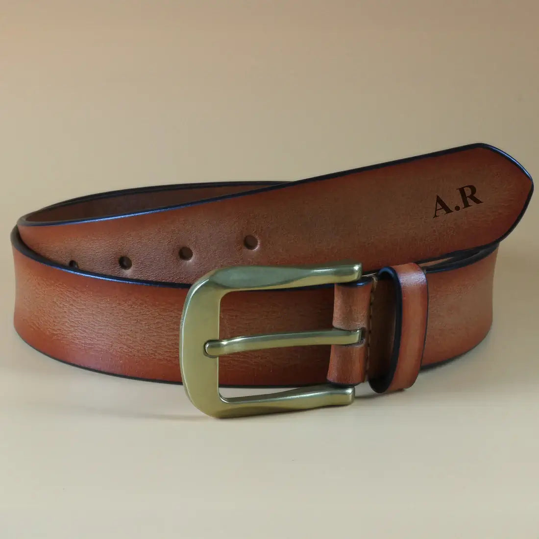 Brown leather men’s belt styled with folded blue clothing showing classic brass buckle