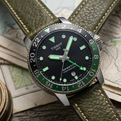 Tissot GMT watch fitted with an olive green leather watch strap featuring matching stitching, styled on vintage maps and outdoor gear to showcase a rugged adventure-inspired look.