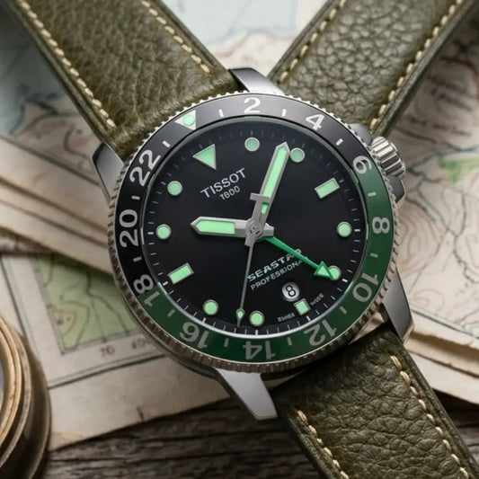Tissot GMT watch fitted with an olive green leather watch strap featuring matching stitching, styled on vintage maps and outdoor gear to showcase a rugged adventure-inspired look.