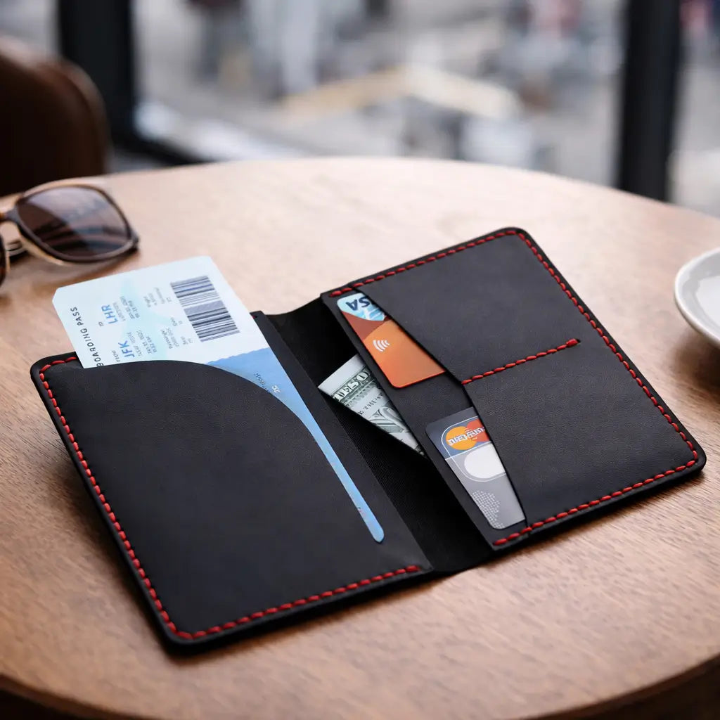 Tactile lifestyle view of a tan full-grain leather bifold card holder held against a soft-focus greenery background, highlighting the natural hide texture and durable artisanal contrast stitching in daylight.