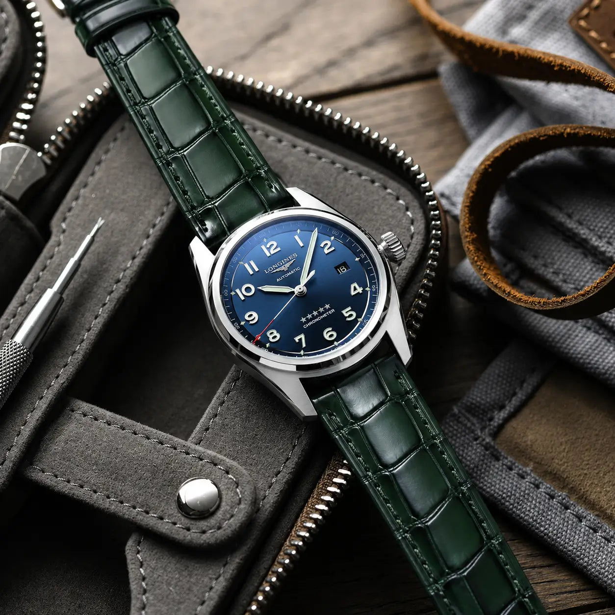 Emerald green crocodile leather watch strap with a high-gloss finish, shown on a blue dial Longines Spirit Chronometer being held by hand.