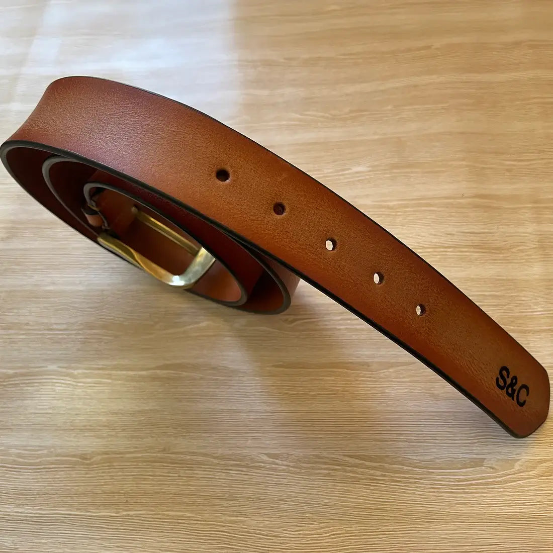 Close-up of brown leather men’s belt showing adjustable holes, edge stitching and personalised initials