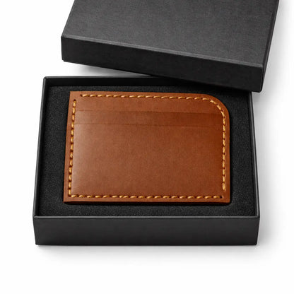 Brown leather cardholder with stitched edges displayed inside an open black gift box with a foam insert.