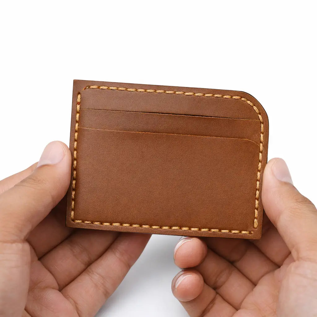 Hands holding a brown leather cardholder with stitched edges against a clean white background.
