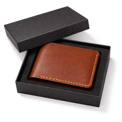 Brown leather bifold wallet with contrast stitching presented inside an open matte black gift box, showcasing a premium gifting setup on a clean neutral background.