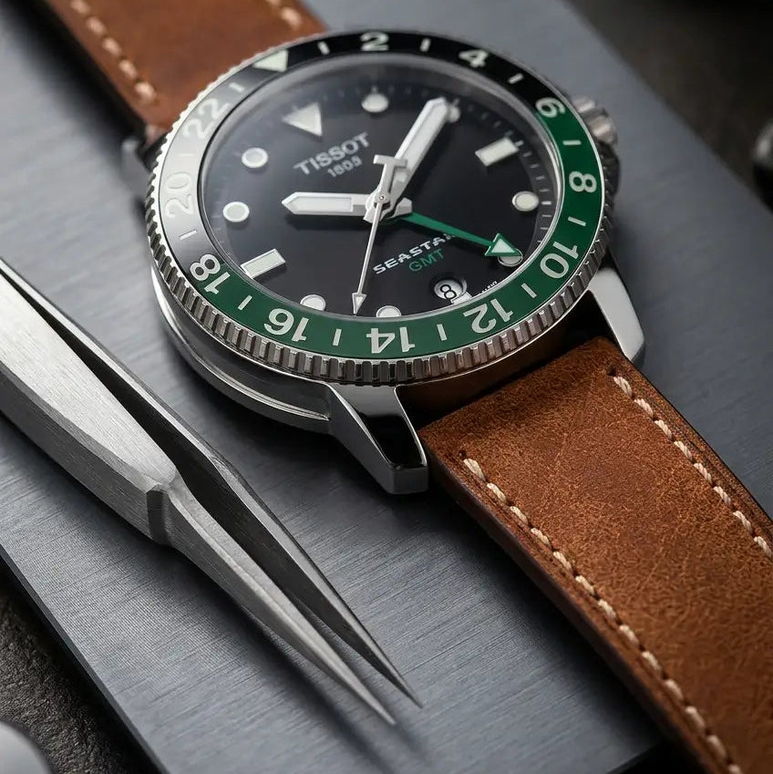 Macro view of a Tissot Seastar GMT watch fitted with a handcrafted brown leather watch strap, displayed beside precision watchmaking tools to highlight premium leather, fine stitching, and artisan craftsmanship.