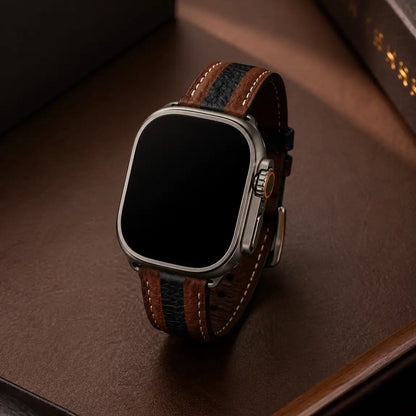 Apple Watch Ultra displayed upright on a rich brown desk surface with the two-tone brown and black leather strap forming a clean curved silhouette. Soft directional lighting emphasizes the leather grain, stitching details, and matte titanium finish. Minimal luxury styling with a dark, refined background. The watch display remains fully off and black.