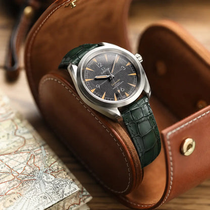 Dark forest green crocodile embossed leather watch strap on an Omega Railmaster, displayed in a brown leather watch roll next to a vintage map.